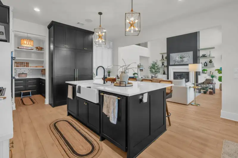 Kitchen with a dark island, a farmhouse sink, dark pantry cabinets, and a view into the living room.
