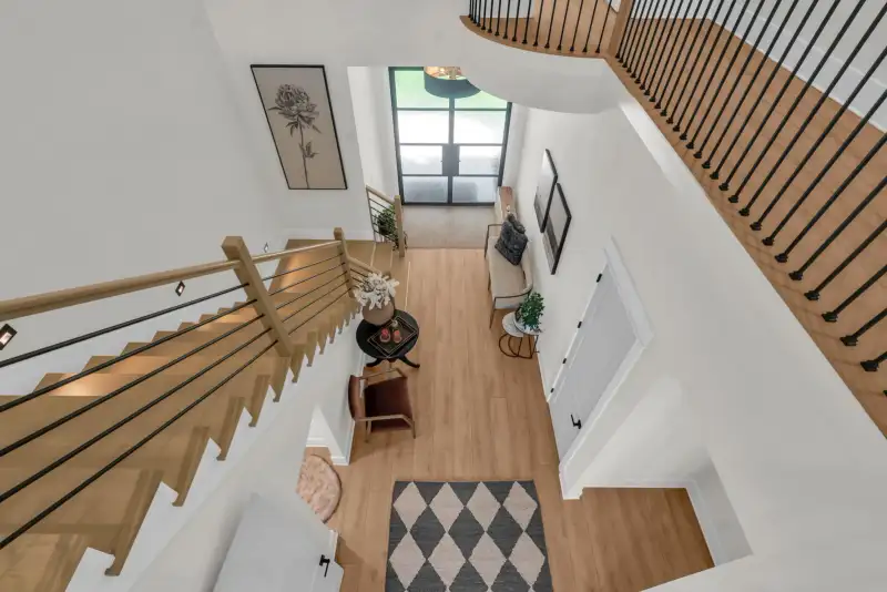 Staircase viewed from above, with a wood handrail, a black-and-white diamond rug, and a front door.