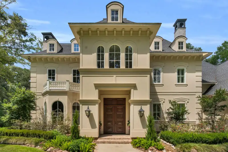 Cream stucco facade with a dark wood double door, wall lanterns, and a balcony above the entry.