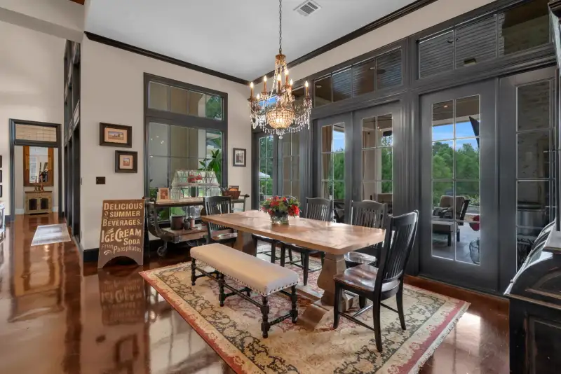 Dining room with a chandelier over a wood table, an upholstered bench, and dark French doors.