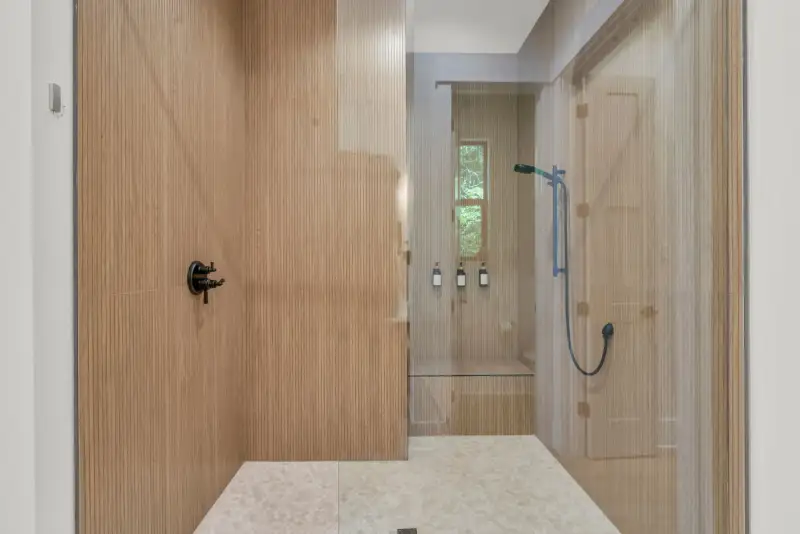 Shower wall with fluted wood panels, a matte black valve, and a glass enclosure.