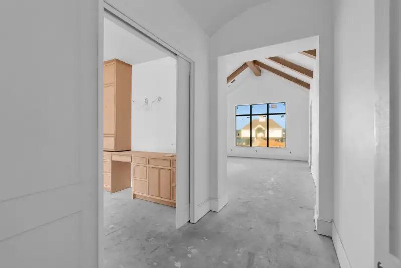 Hallway with a sliding door to a built-in desk room and an arched opening to a room with exposed beams.