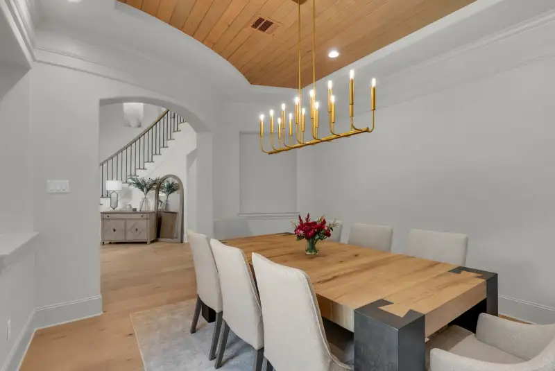 Dining room with a wood plank ceiling, a gold chandelier, and a view of a staircase with iron balusters.