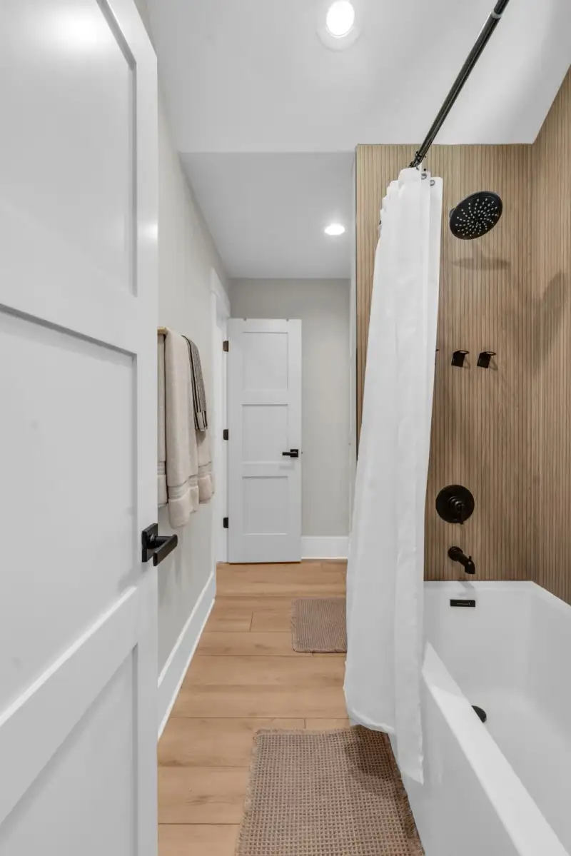 Tub and shower with a white shower curtain, a wood wall panel, and black fixtures.
