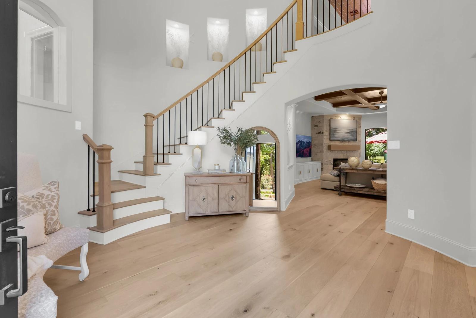Two-story foyer with a curved staircase, light wide-plank hardwood floors, and an arched doorway into the living room.