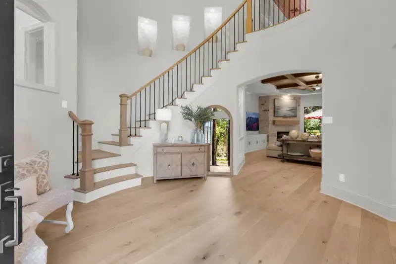 Two-story foyer with a curved staircase, light wide-plank hardwood floors, and an arched doorway into the living room.