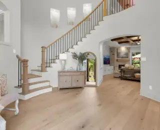 Two-story foyer with a curved staircase, light wide-plank hardwood floors, and an arched doorway into the living room.