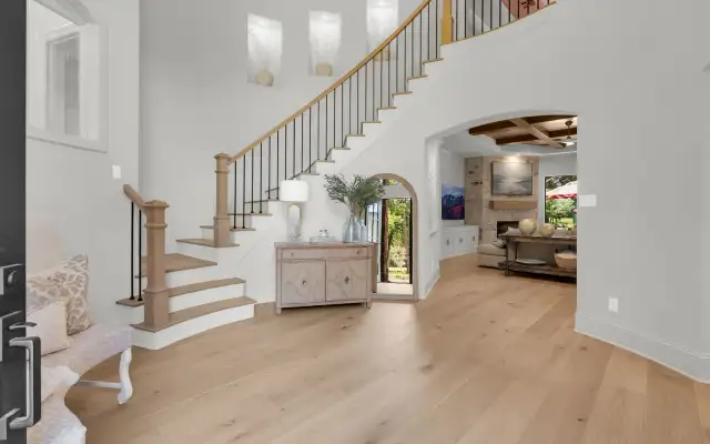 Two-story foyer with a curved staircase, light wide-plank hardwood floors, and an arched doorway into the living room.