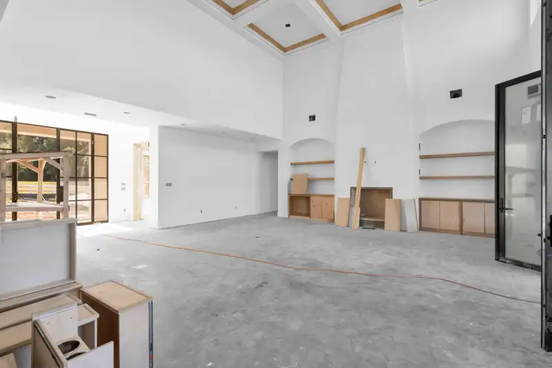 Two-story room with a coffered ceiling, built-in shelves, and a tall black-framed glass door at right.