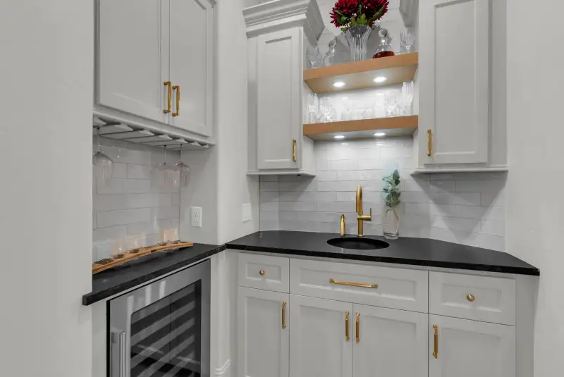 Bar area with a wine refrigerator, a stemware rack, a dark countertop, and a gold faucet over a sink.