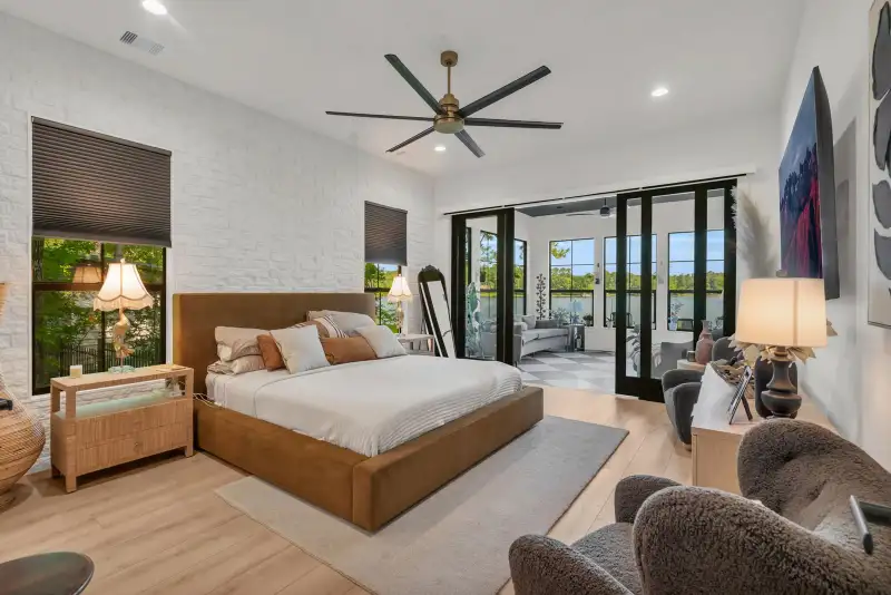 Primary bedroom with a brown upholstered bed, white brick accent wall, and sliding glass doors to an adjoining sitting area.