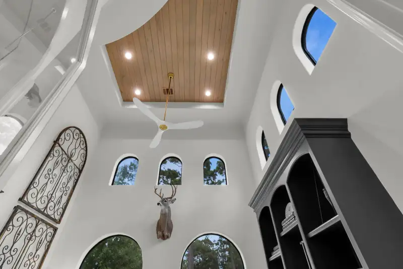 Upward view of a two-story room with a wood plank ceiling, arched windows, and a mounted deer head.