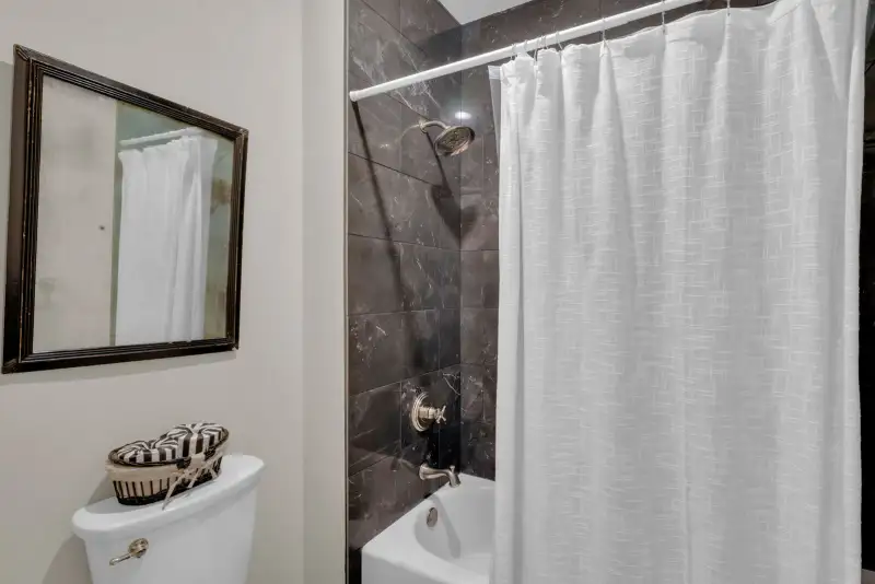Bathroom with a framed mirror, a dark tile tub surround, and a white shower curtain.