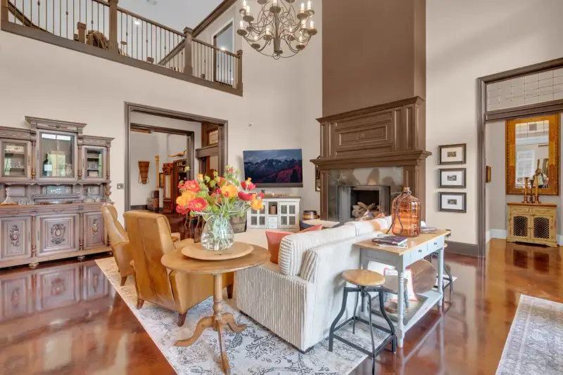 Two-story living room with a wood-surround fireplace, a striped sofa, a round wood table, and a balcony rail.