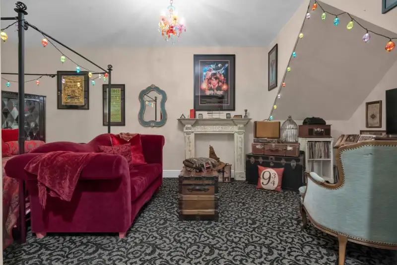 Bedroom with a deep red velvet sofa, a black iron canopy bed with string lights, and a white fireplace mantel.