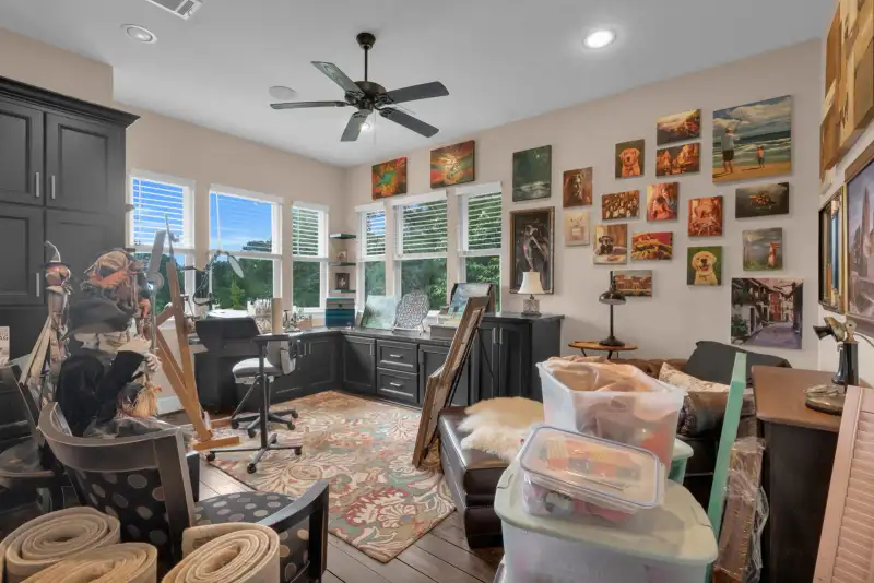 Room with a gallery wall of framed paintings, dark cabinets, a desk, and a ceiling fan.