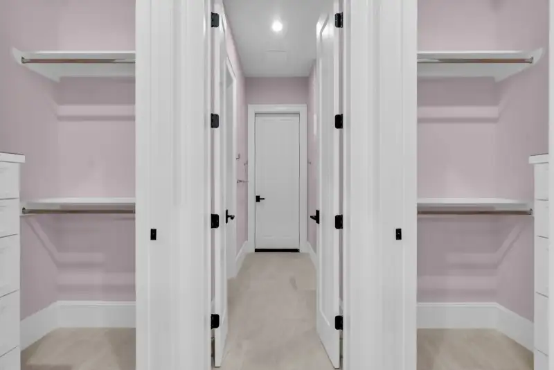 Walk-in closets with white shelving and pink walls, with a white door at the far end.