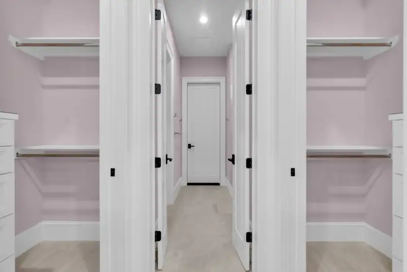 Walk-in closets with white shelving and pink walls, with a white door at the far end.
