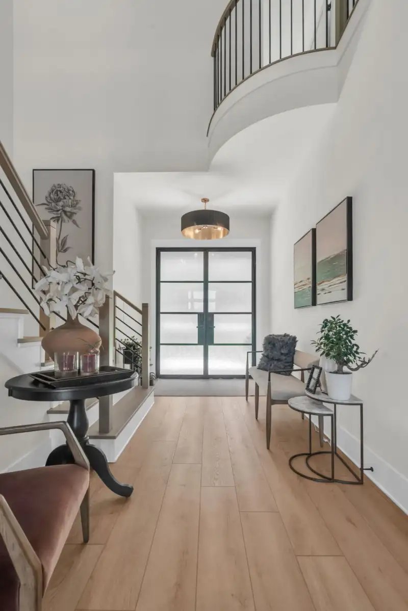 Foyer with a curved staircase, a glass double door, a round side table, and light oak flooring.