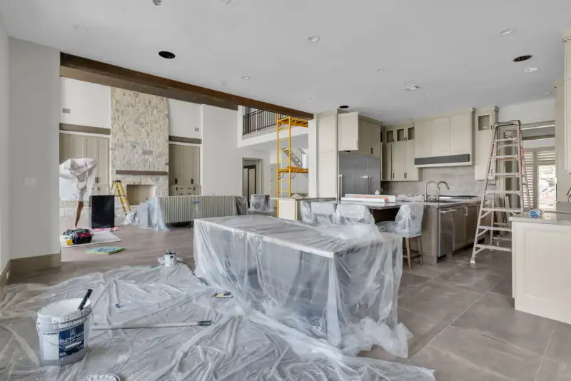 Kitchen and great room under construction, with a plastic-covered island and a bucket on the floor.