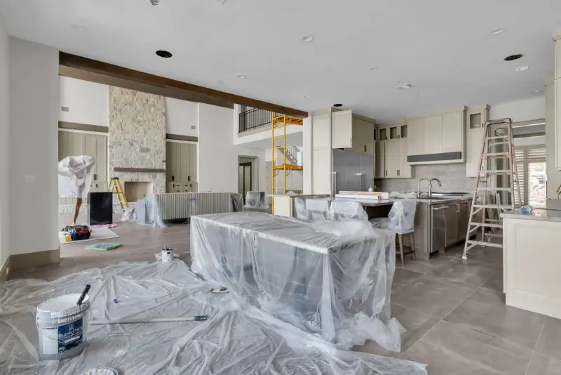 Kitchen and great room under construction, with a plastic-covered island and a bucket on the floor.