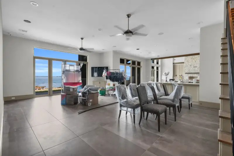 Living area with lake-facing glass doors, ceiling fans, and dining chairs under plastic covers.