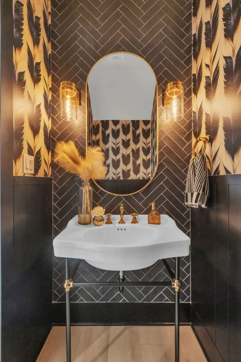 Powder room with a white console sink on black legs, brass faucet, and herringbone tile behind an oval mirror.