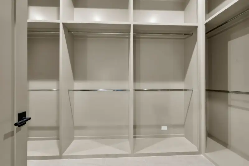 Walk-in closet with open shelving, hanging rods, and a black door handle at the left.