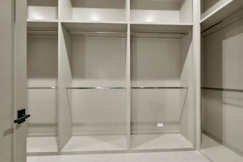 Walk-in closet with open shelving, hanging rods, and a black door handle at the left.