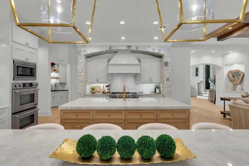 Kitchen island with gold pendant lanterns, a stone arch over the cooktop, and a double wall oven.