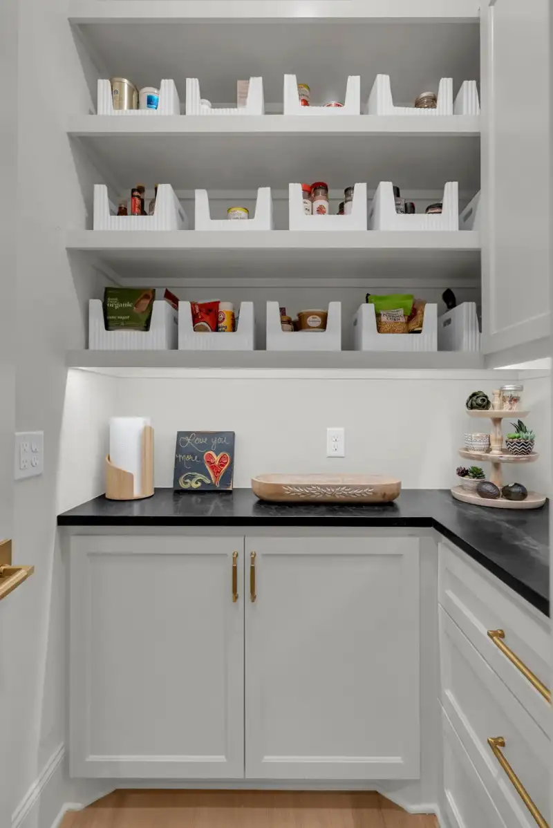 Pantry with white bin organizers on open shelves, a black countertop, and a paper towel holder.