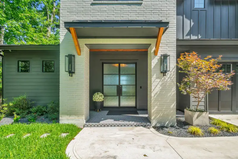 Covered front entry with a glass double door, gray brick walls, and wood beam accents.