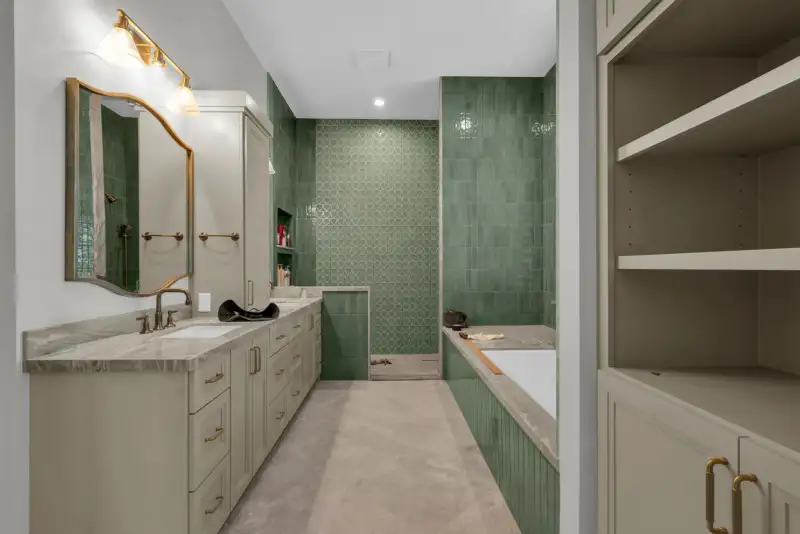 Bathroom with green tile, a brass-framed mirror, and a vanity with gold fixtures.