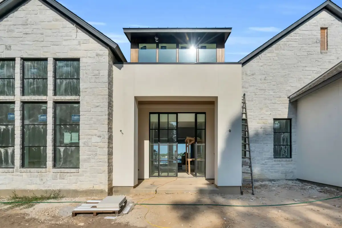 Entry of a stone-clad house with black-framed glass doors and a glass railing on the upper level.