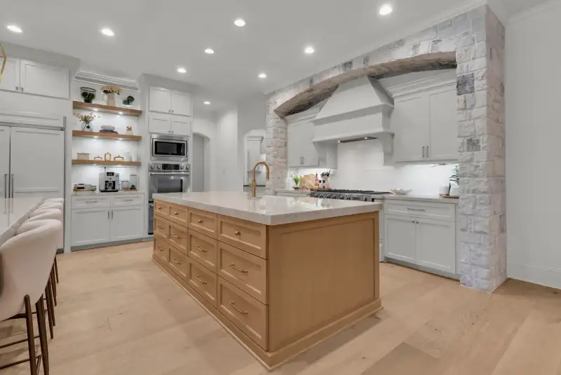 Kitchen island with a marble-look top, light wood base, and a stone arch over the cooktop.