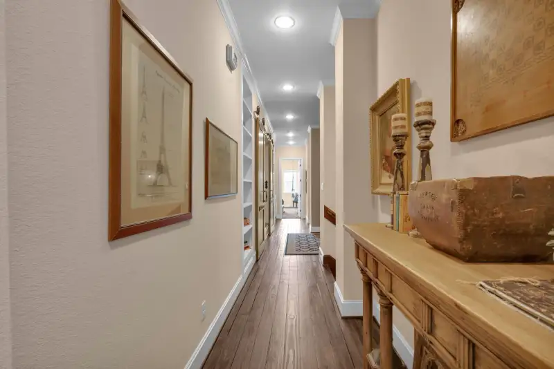 Hallway with framed prints, built-in shelving, wood floors, and a wood console table with candlesticks.