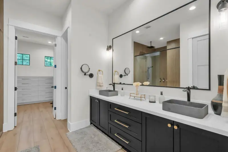 Bathroom vanity with gray vessel sinks, a doorway into a walk-in closet, and a black-framed mirror.