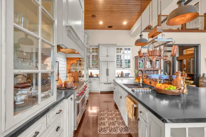 White kitchen with glass-front cabinets, a built-in range, a dark countertop, and a copper pot rack overhead.