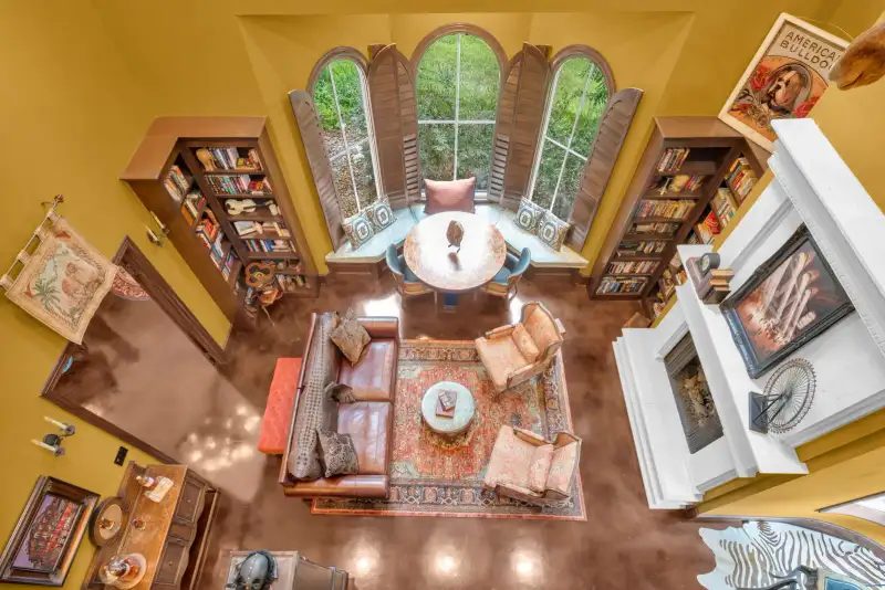 Overhead view of a yellow-walled sitting room with a leather sofa, armchairs, bookshelves, and a white fireplace.