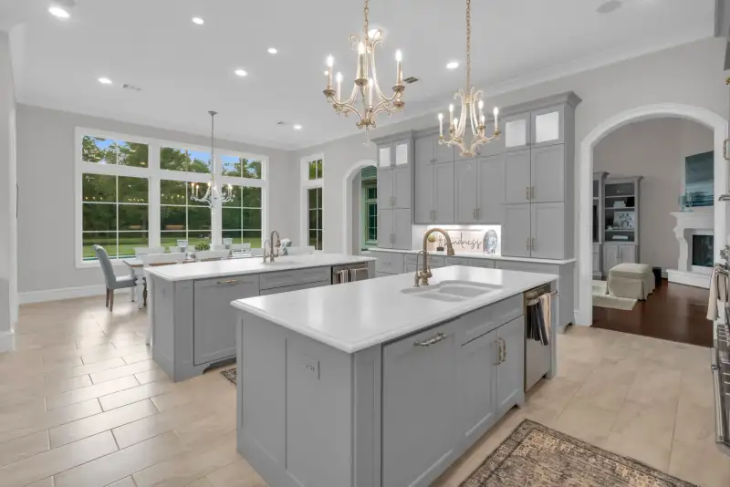 Kitchen with two islands, twin chandeliers, gray cabinets, and an arched doorway to the living room.