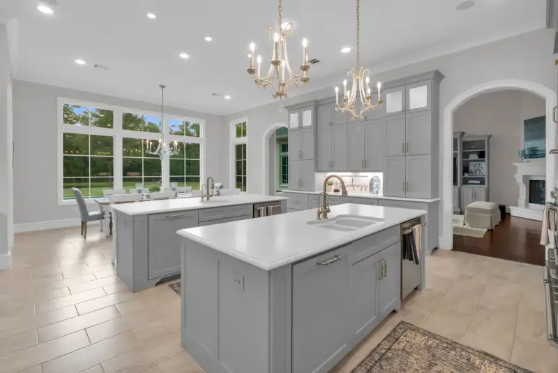 Kitchen with two islands, twin chandeliers, gray cabinets, and an arched doorway to the living room.
