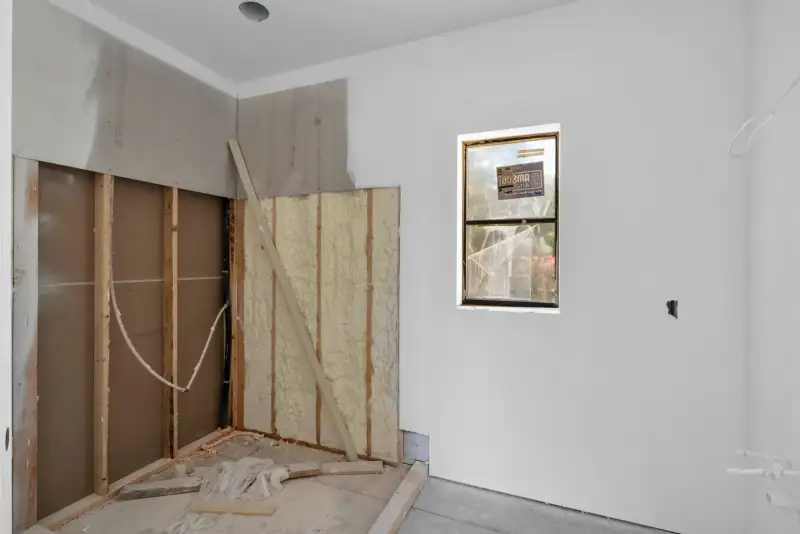Unfinished room with spray foam insulation exposed in an open wall cavity and a small window.