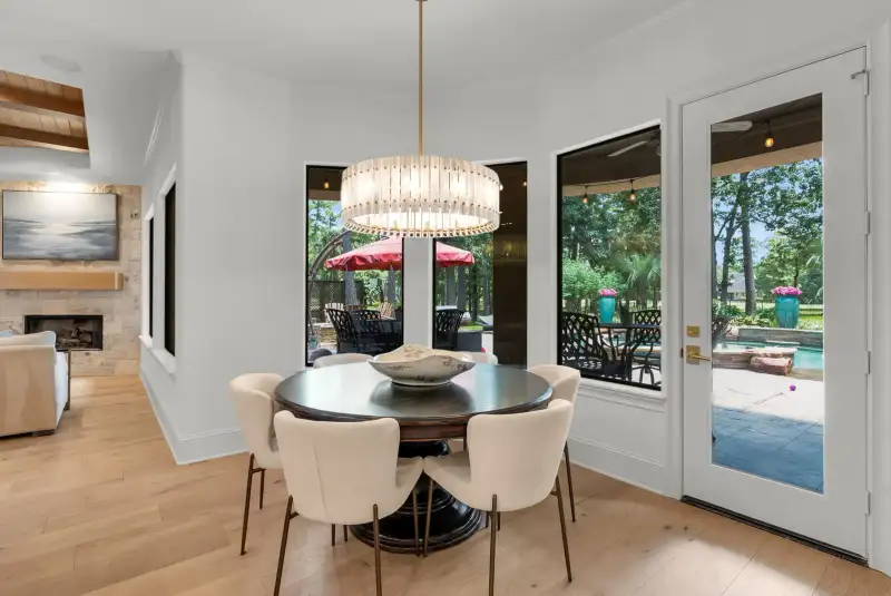 Breakfast nook with a round table, upholstered chairs, a stone fireplace, and doors to a covered patio and pool.