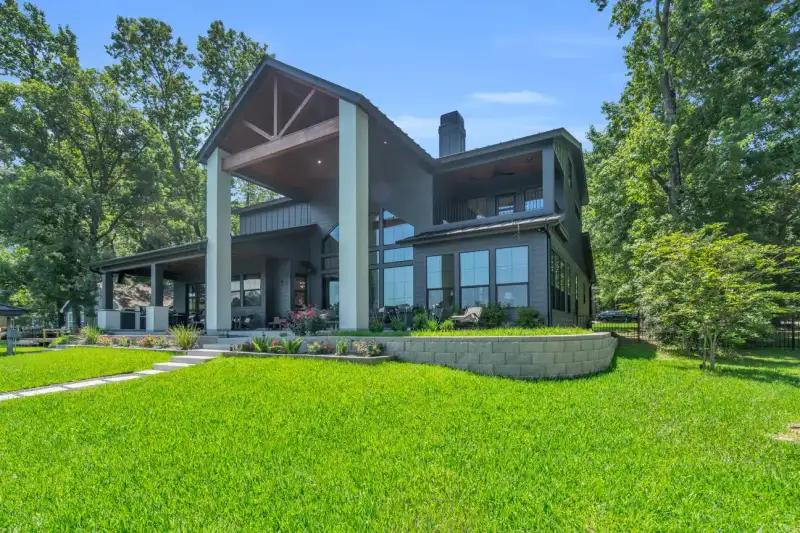 Rear view of the home with a gabled roof, tall columns, and a sloped lawn.