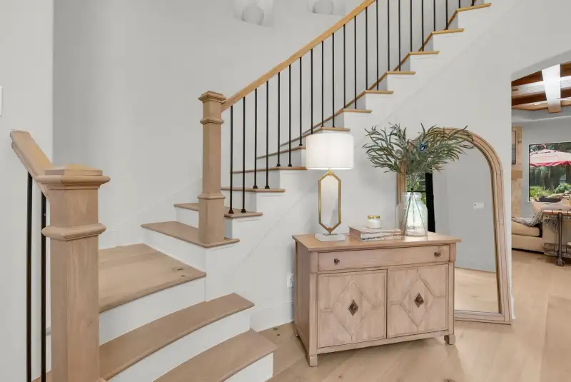 Staircase with wood treads, black iron balusters, and a console table beneath an arched mirror.