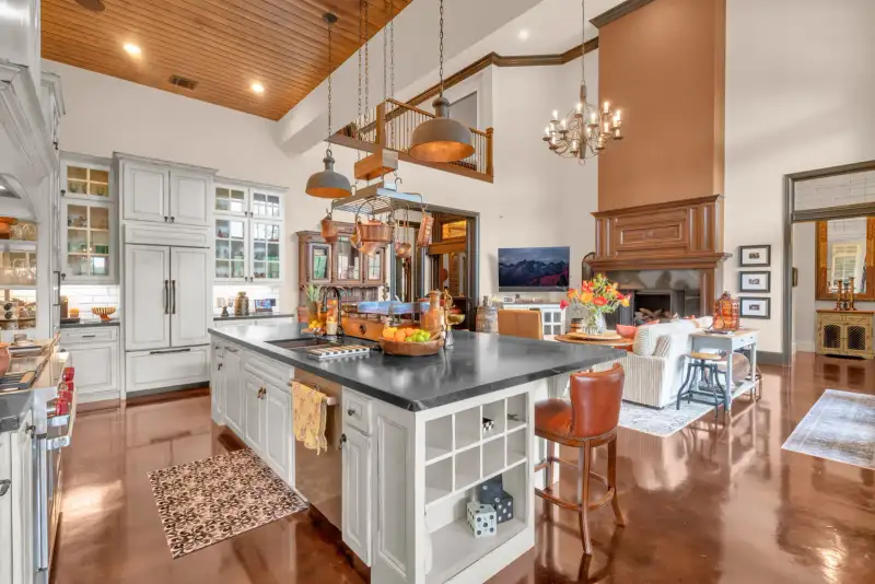 Kitchen island with a dark countertop and a leather bar stool, open to a living room with a wood fireplace.