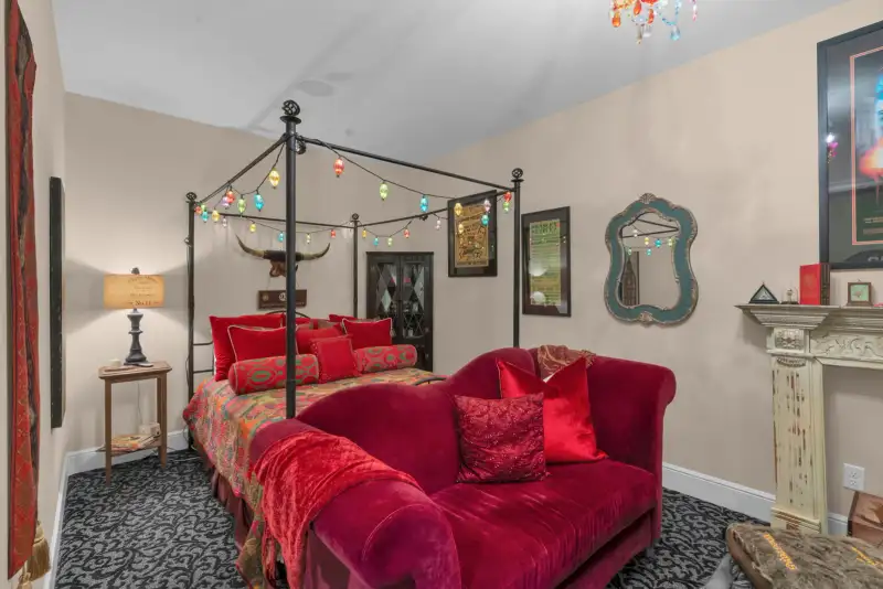 Bedroom with a black iron canopy bed, a longhorn skull above the headboard, a red velvet sofa, and string lights.
