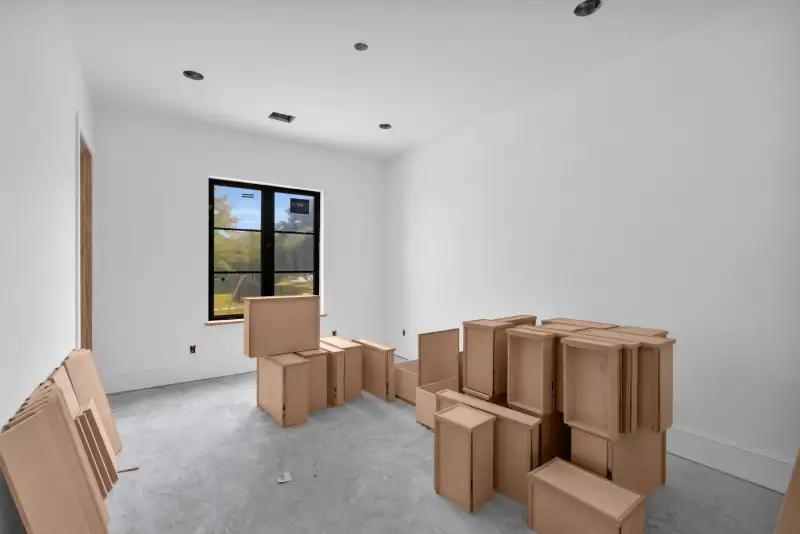 Unfinished room with stacked cardboard cabinet boxes and a black-framed window looking out to trees.