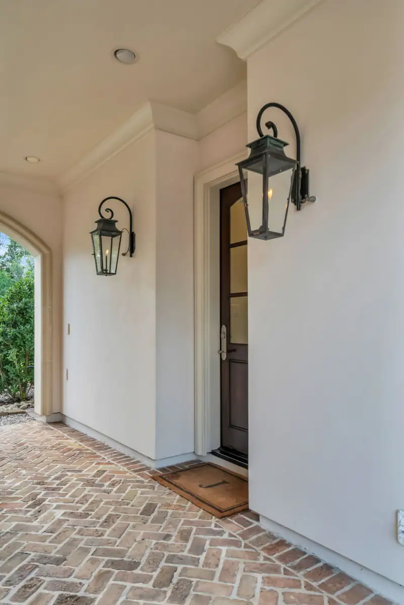 Entry with a glass-paneled dark wood door, two wall lanterns, and a brick floor.
