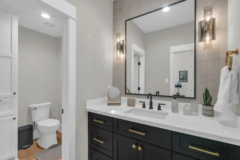 Bathroom vanity with dark cabinets, a large framed mirror, and a toilet visible through an open door.